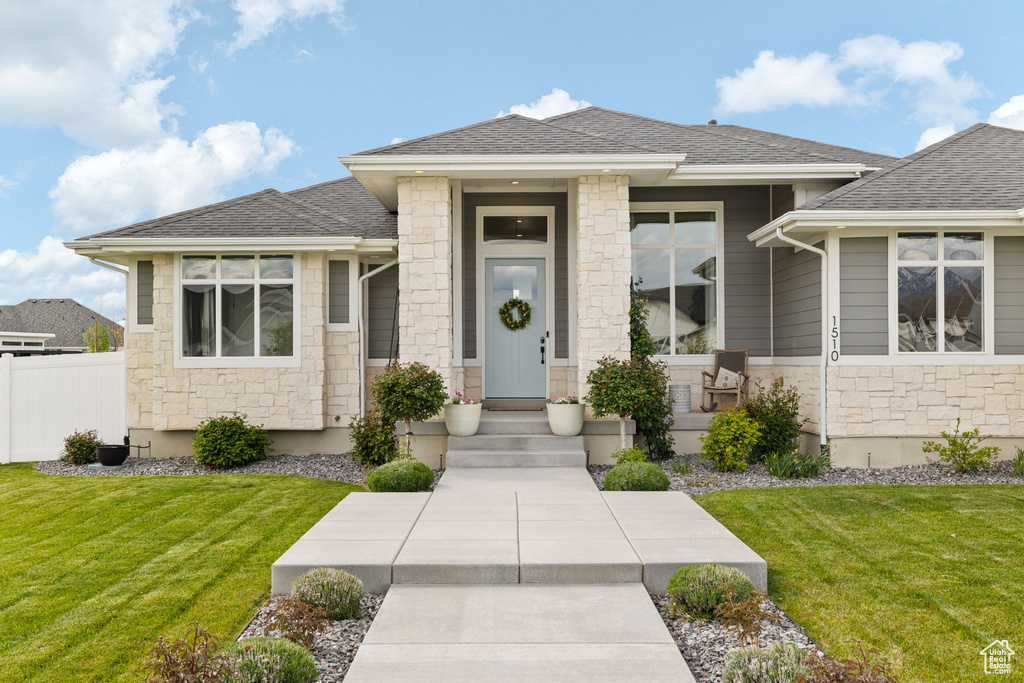 Prairie-style home with a front lawn, a shingled roof, and stone siding