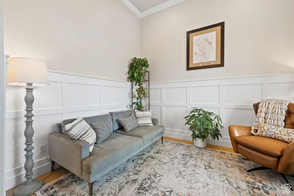 Living area with ornamental molding, a wainscoted wall, wood finished floors, and a decorative wall