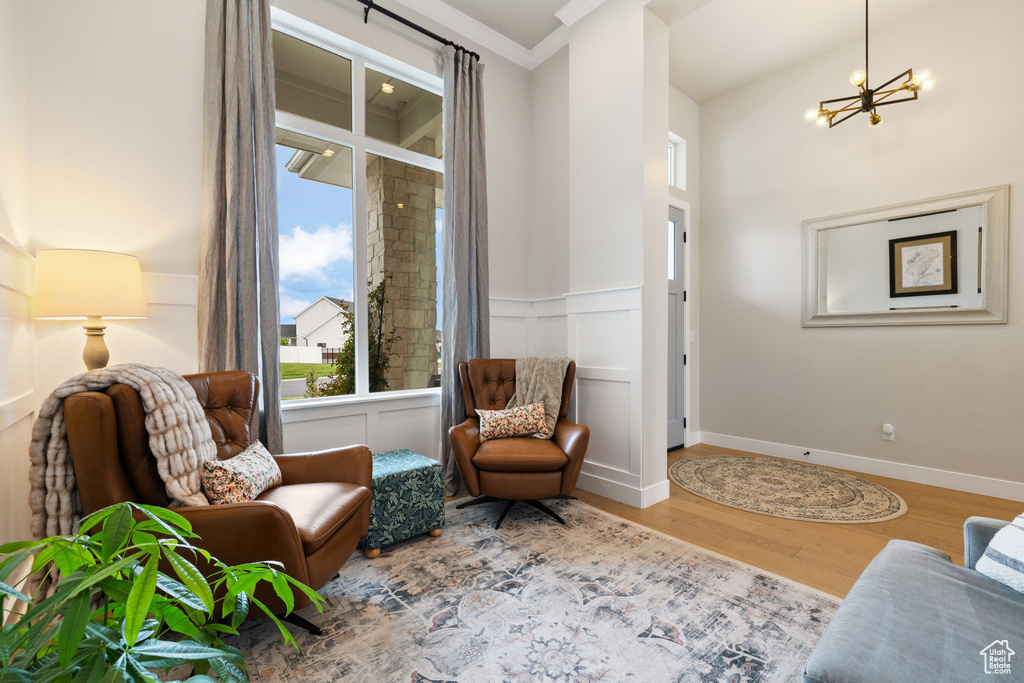 Living area featuring wood finished floors, a decorative wall, a chandelier, ornamental molding, and a wainscoted wall