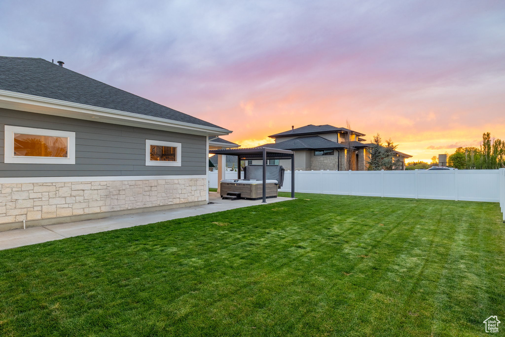 Yard at dusk with a gazebo, a fenced backyard, a patio, and a hot tub