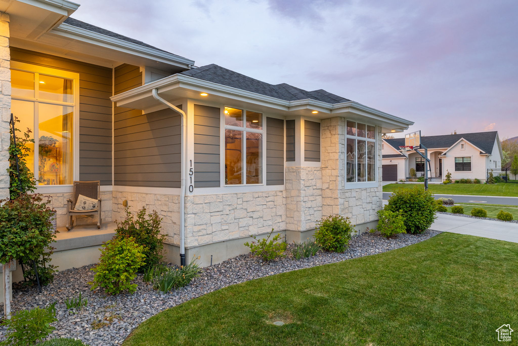 Property exterior at dusk with a lawn, roof with shingles, and stone siding