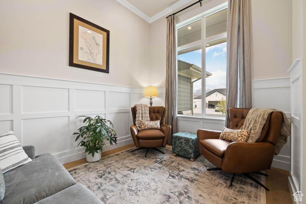 Living area featuring wood finished floors, a decorative wall, a wainscoted wall, and ornamental molding