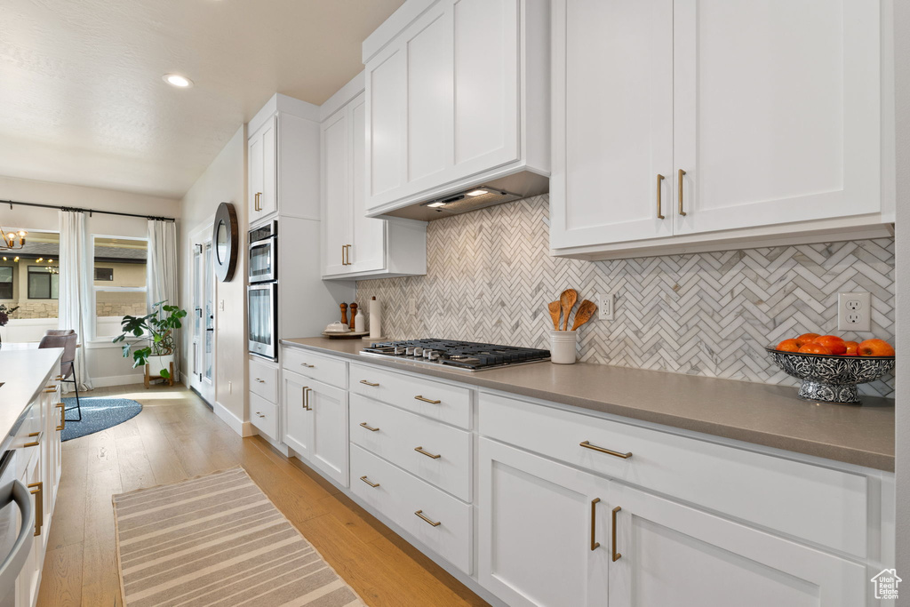 Kitchen featuring white cabinetry, light wood-type flooring, stainless steel appliances, and tasteful backsplash