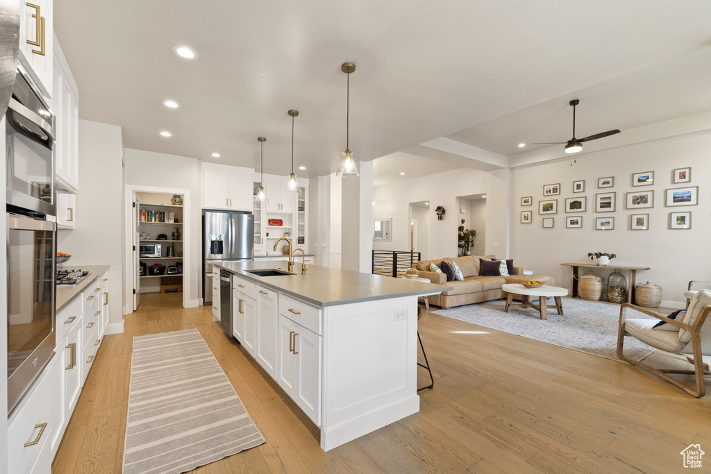 Kitchen featuring white cabinetry, a sink, appliances with stainless steel finishes, open floor plan, and a ceiling fan