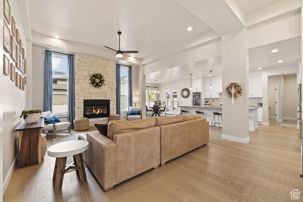 Living area featuring ceiling fan, a stone fireplace, light wood finished floors, and plenty of natural light