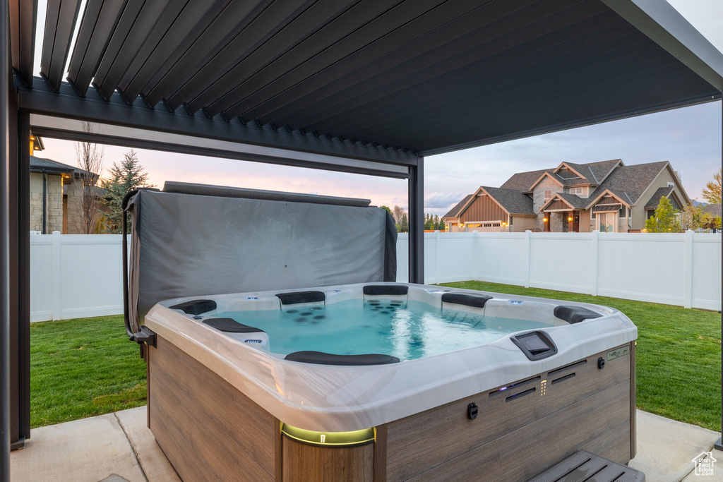 Patio terrace at dusk with a fenced backyard, a hot tub, and a yard