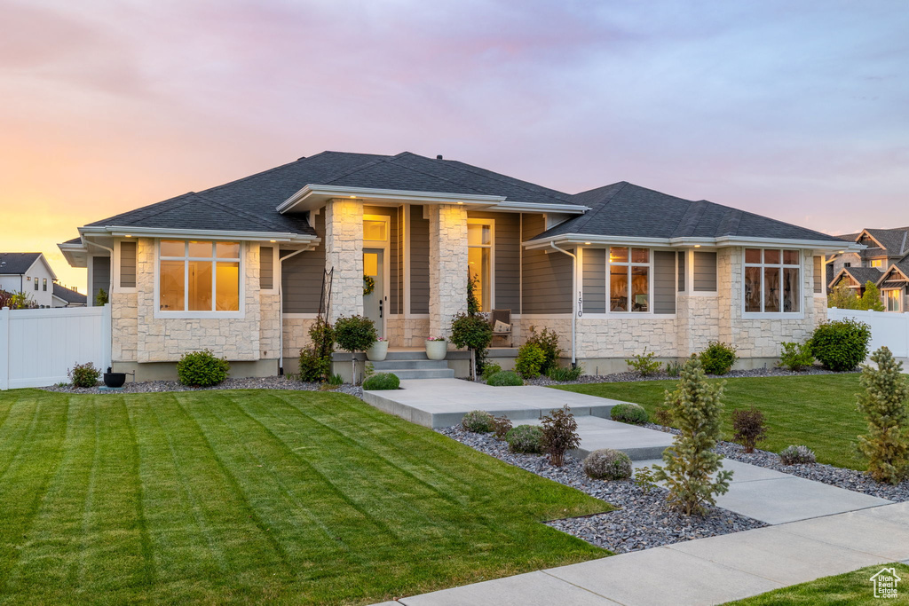 Prairie-style house featuring fence, a yard, a shingled roof, and stone siding