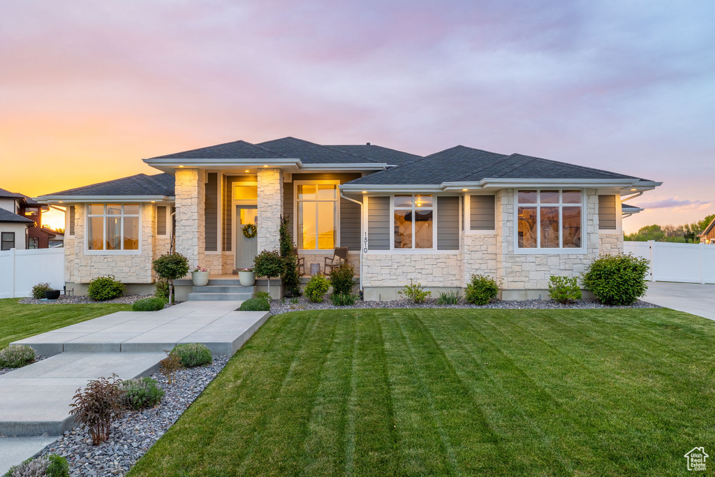 Prairie-style house with a front yard, stone siding, a shingled roof, and fence