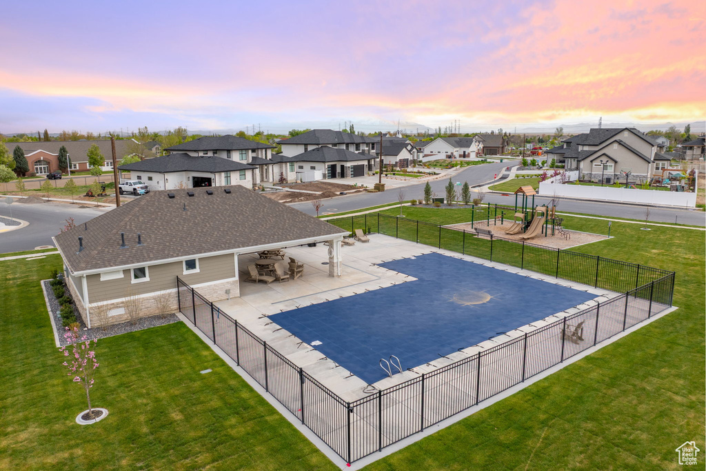 Pool at dusk featuring fence, a residential view, and a lawn