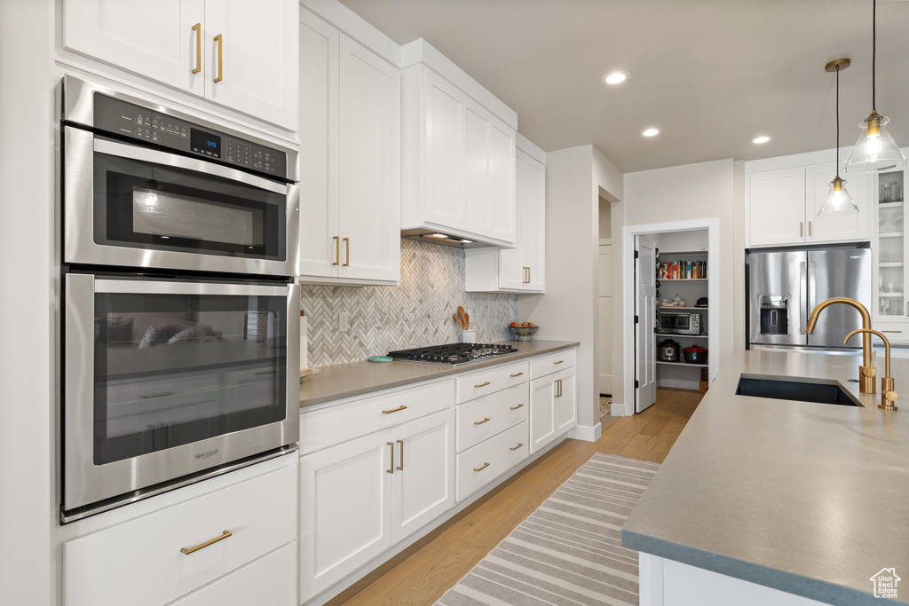 Kitchen featuring a sink, light wood-style flooring, backsplash, white cabinets, and appliances with stainless steel finishes