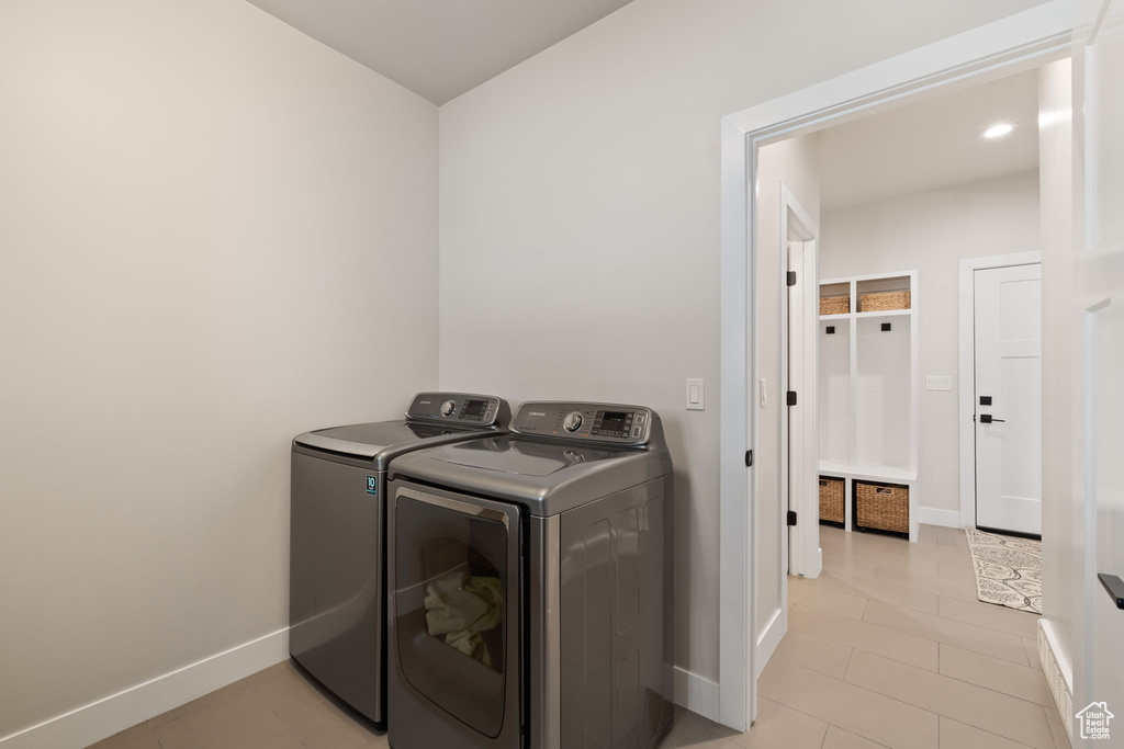 Clothes washing area featuring light tile patterned flooring, independent washer and dryer, laundry area, and baseboards