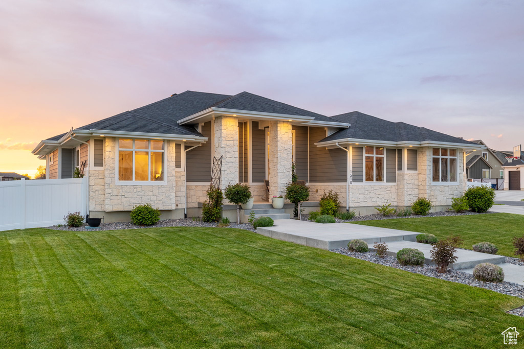 Prairie-style home with a lawn, fence, and stone siding