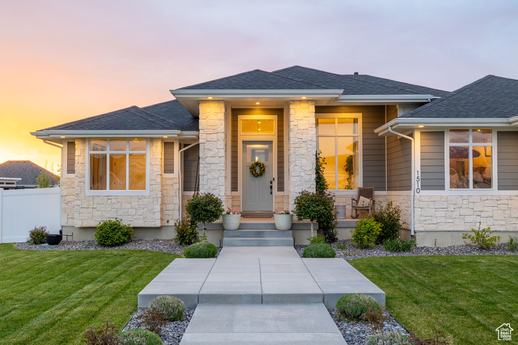 Prairie-style home with a yard, stone siding, a shingled roof, and fence