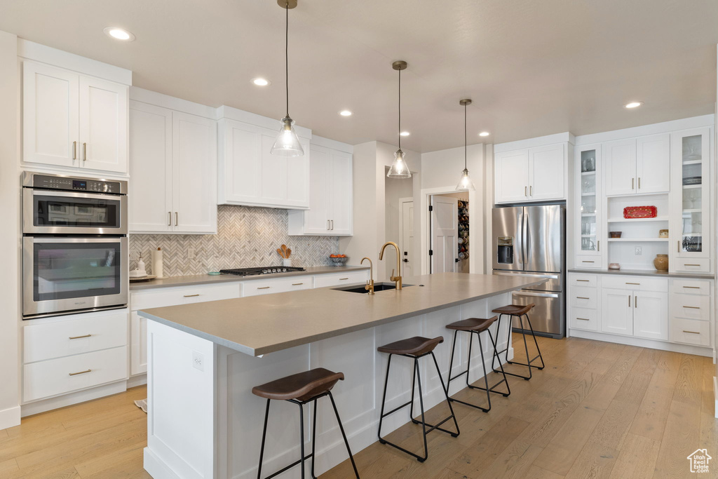 Kitchen featuring light wood finished floors, a sink, stainless steel appliances, decorative backsplash, and a breakfast bar