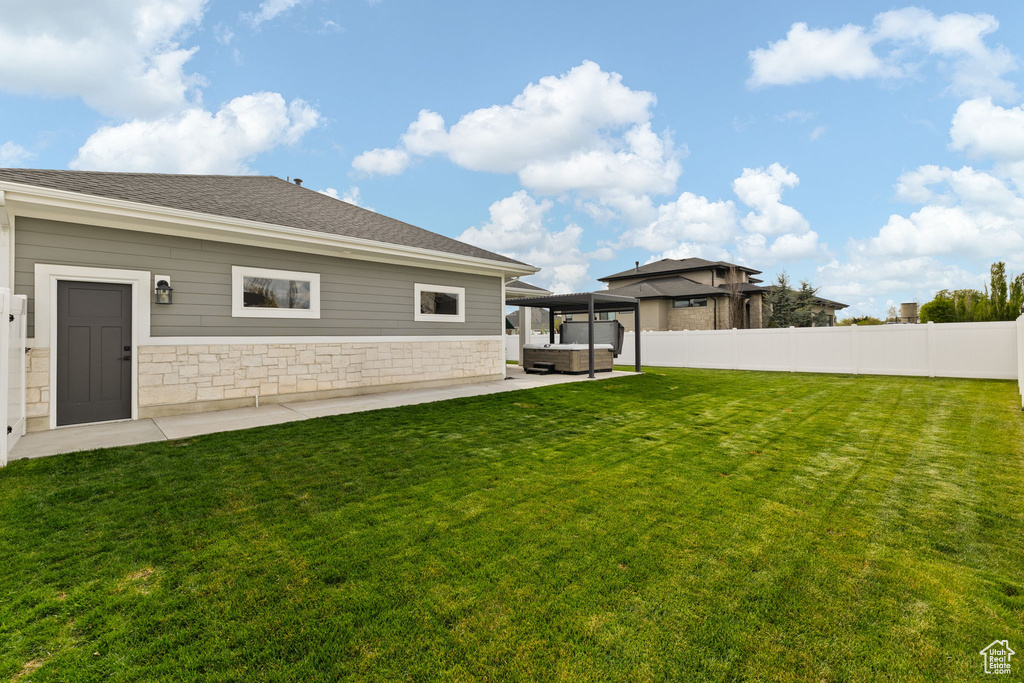 Rear view of property with a lawn, stone siding, a hot tub, and fence