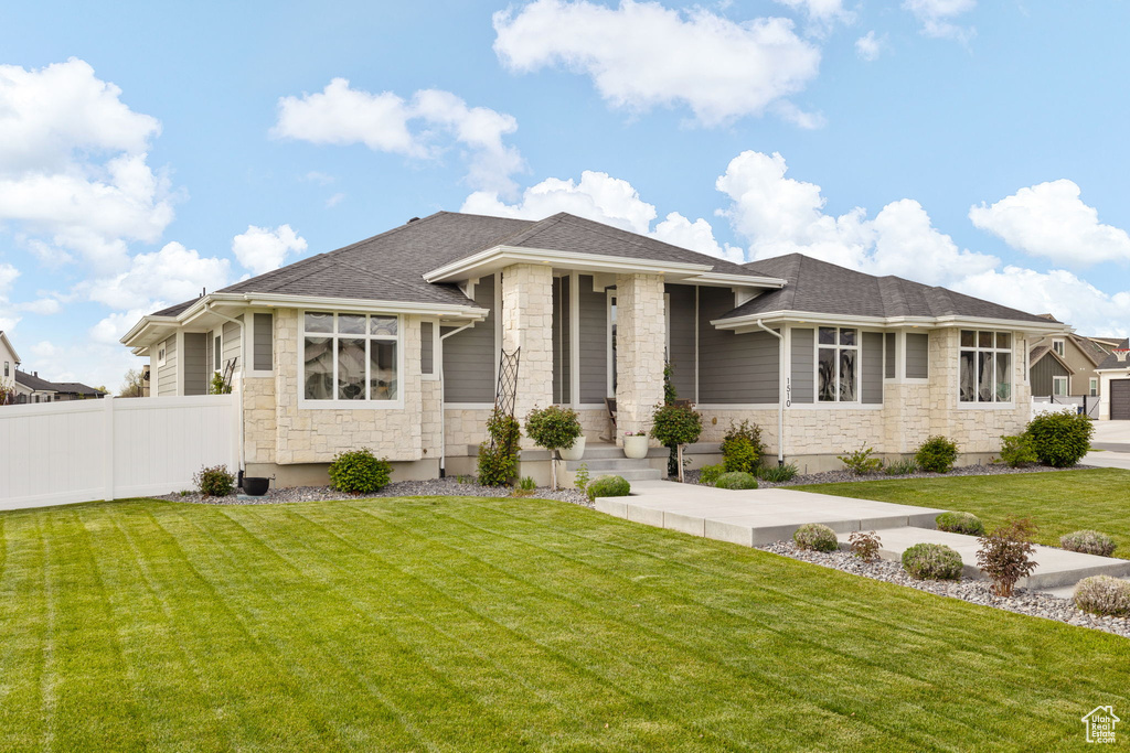 Prairie-style home with a shingled roof, fence, a front lawn, and stone siding