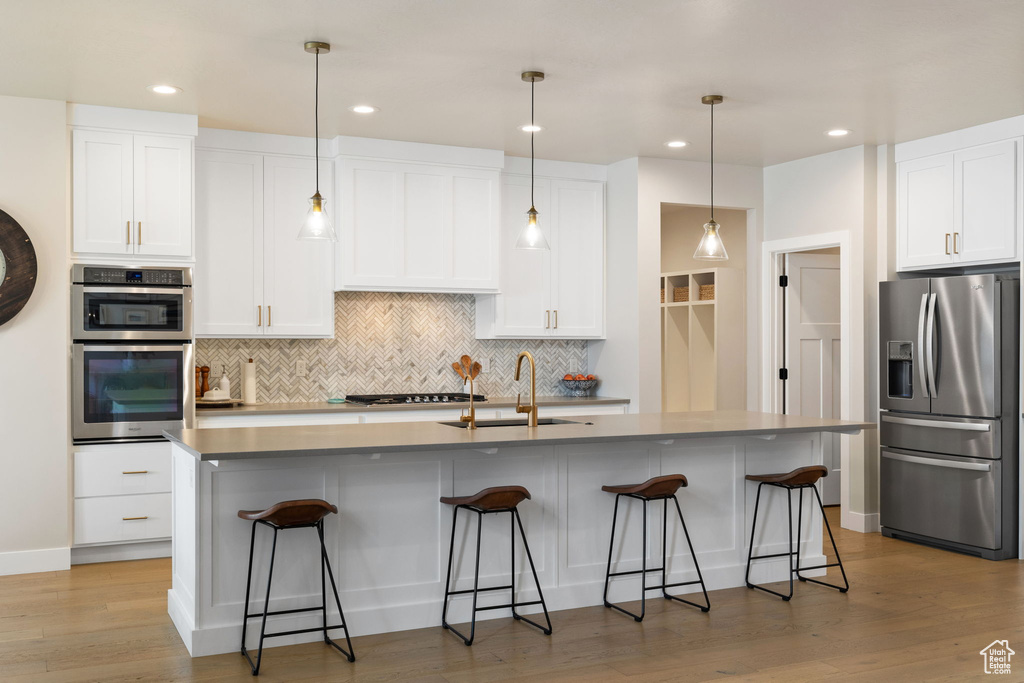 Kitchen featuring white cabinets, appliances with stainless steel finishes, decorative backsplash, and a sink