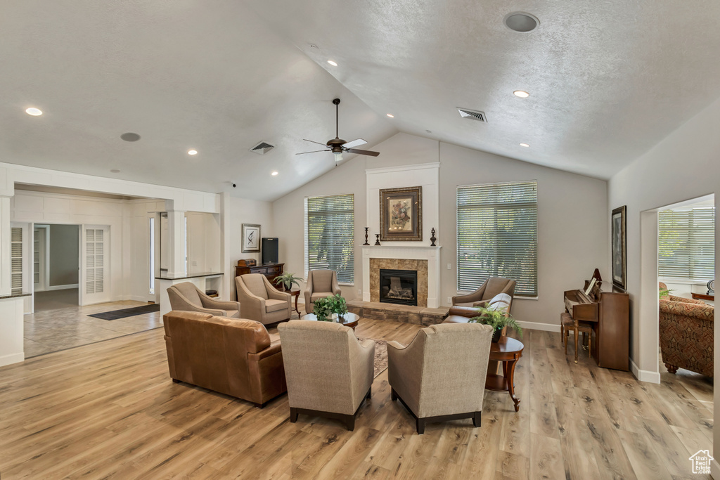 Living room with light wood finished floors, a glass covered fireplace, lofted ceiling, and a wealth of natural light