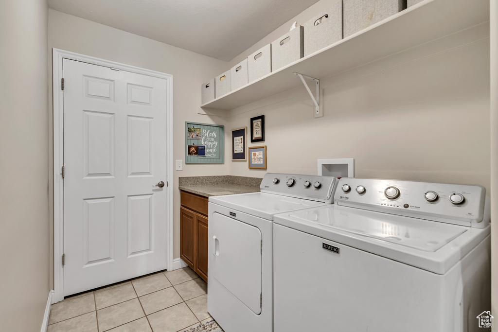 Clothes washing area with separate washer and dryer, baseboards, cabinet space, and light tile patterned floors