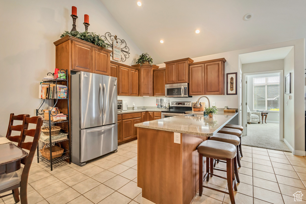 Kitchen featuring brown cabinetry, a peninsula, a sink, light tile patterned floors, and stainless steel appliances