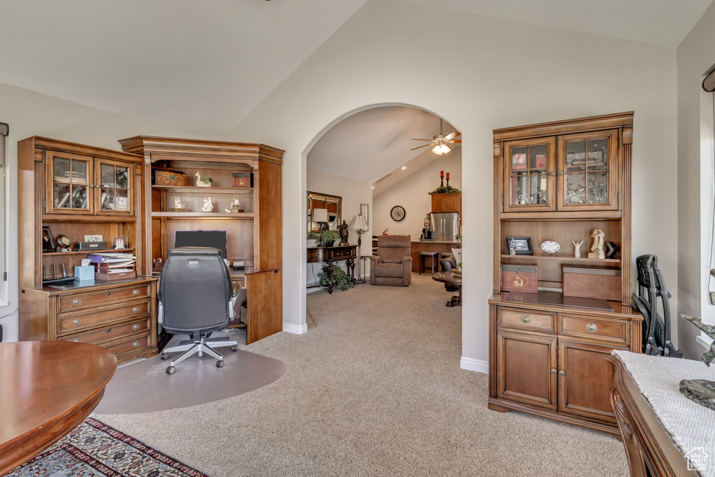 Office area with ceiling fan, light carpet, arched walkways, baseboards, and vaulted ceiling