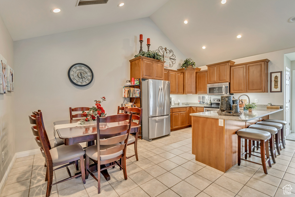 Kitchen featuring appliances with stainless steel finishes, light tile patterned flooring, a peninsula, and high vaulted ceiling