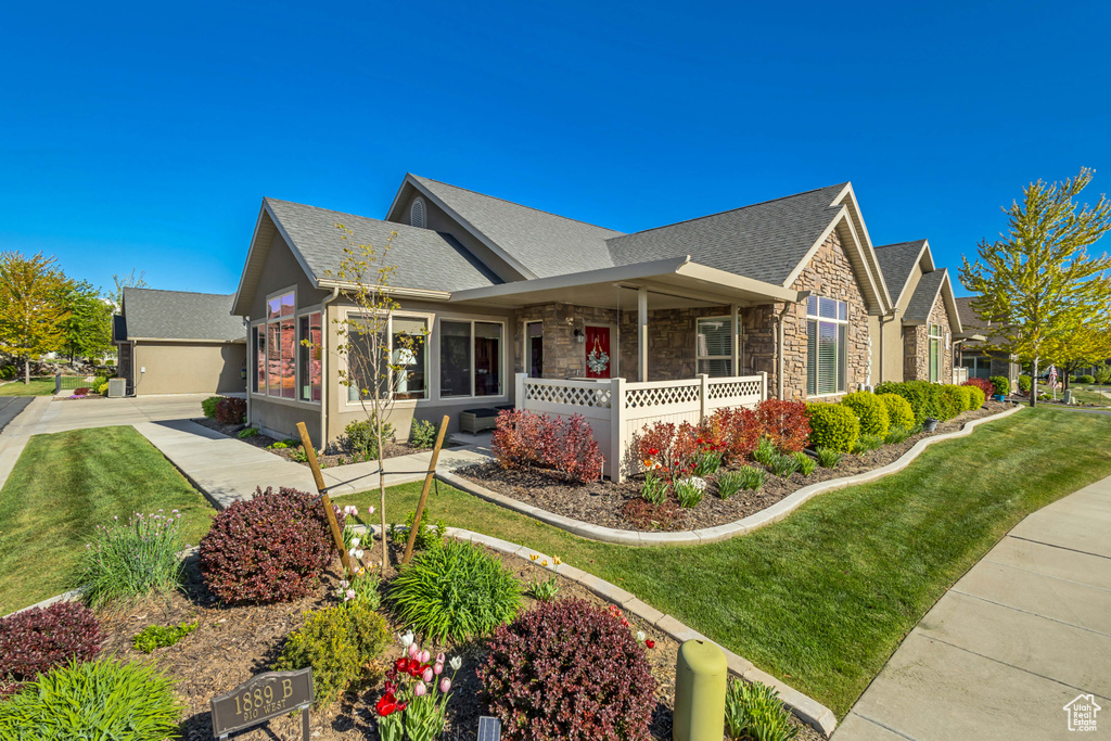 View of front of house featuring a porch, a shingled roof, stone siding, and a front lawn