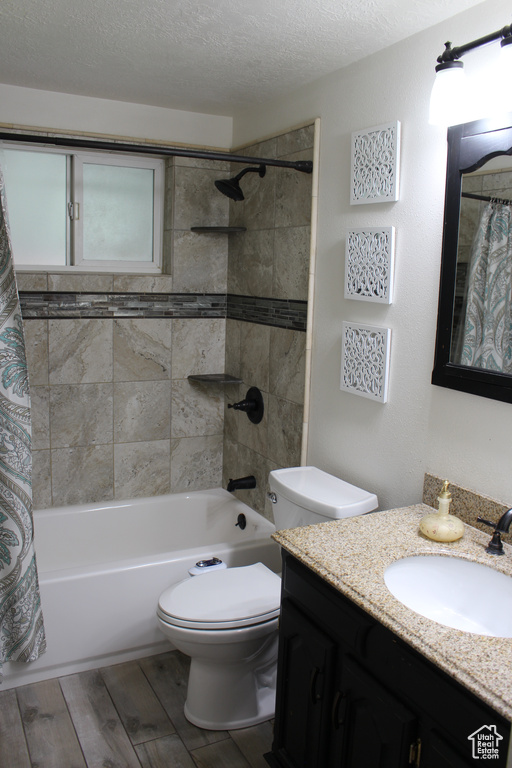 Full bathroom with a textured ceiling, shower / bath combination with curtain, wood finished floors, vanity, and toilet