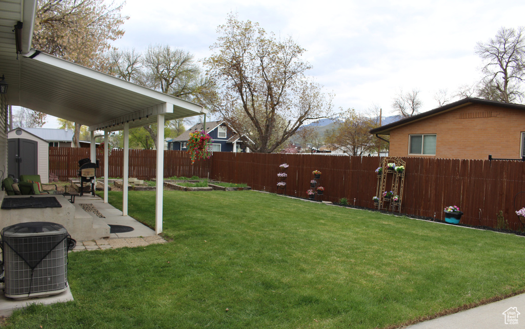 View of yard with a storage unit, a fenced backyard, an outbuilding, cooling unit, and a patio area