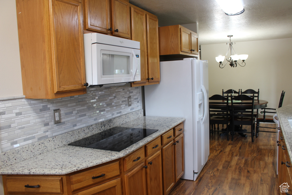 Kitchen featuring brown cabinets, an inviting chandelier, white appliances, backsplash, and dark wood-style floors