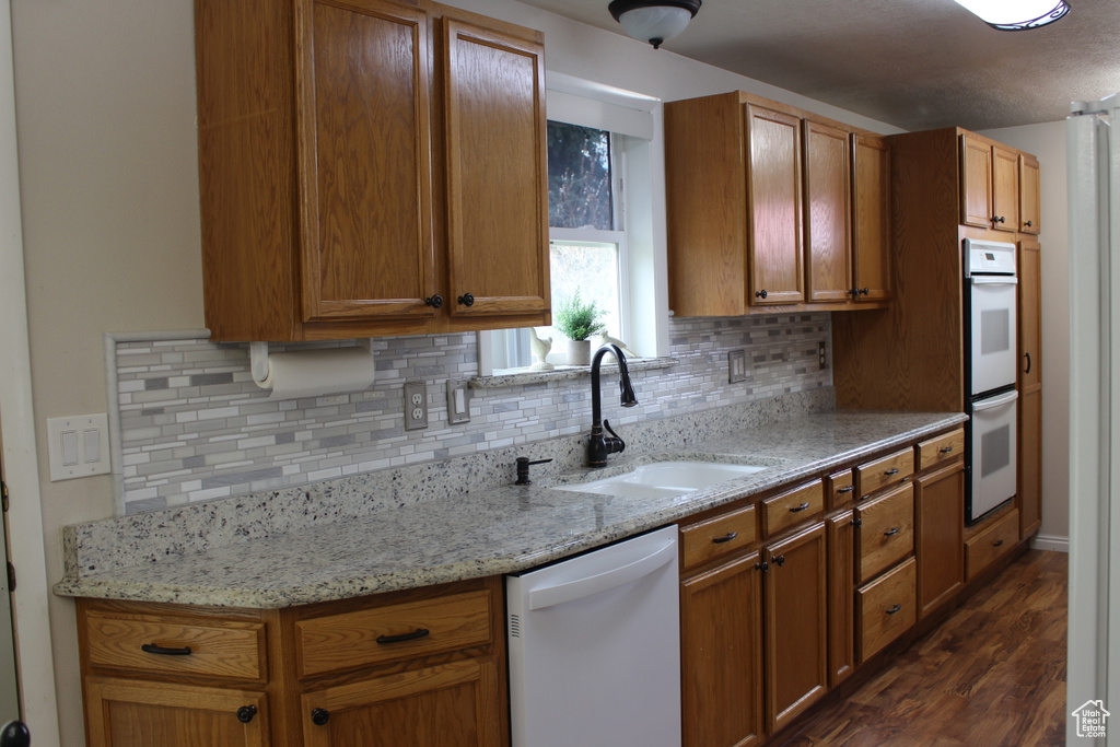 Kitchen featuring a sink, decorative backsplash, white appliances, and dark wood-type flooring