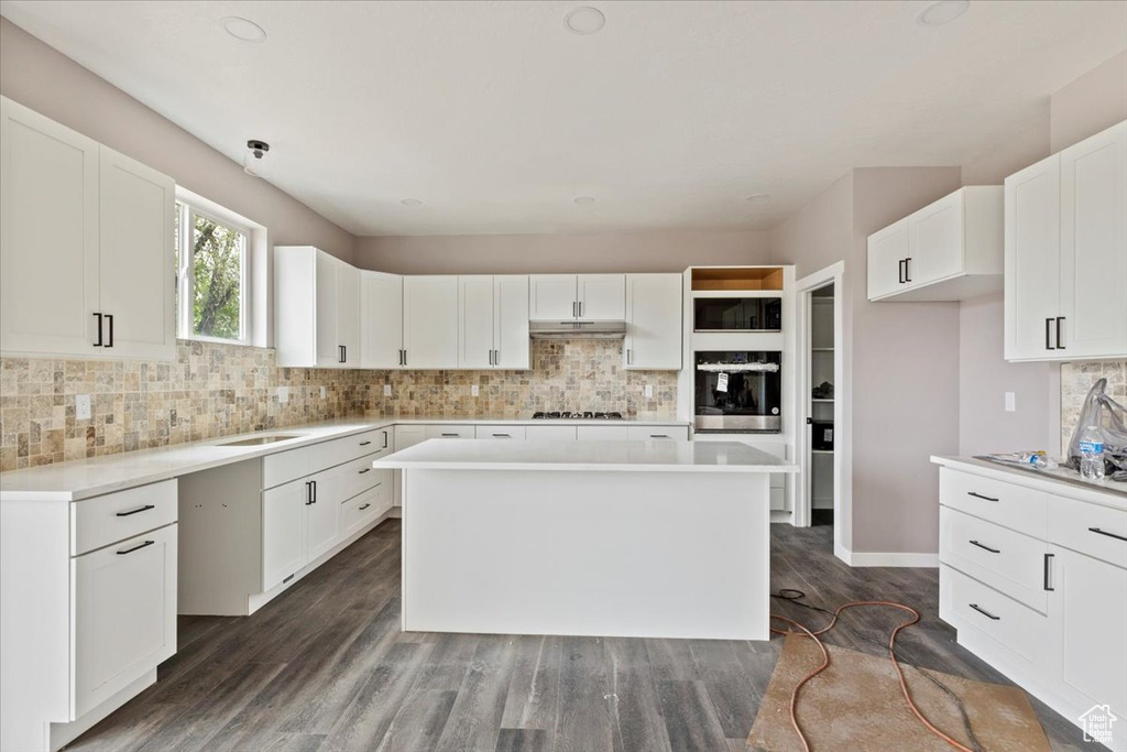 Kitchen with under cabinet range hood, stainless steel oven, gas cooktop, and tasteful backsplash