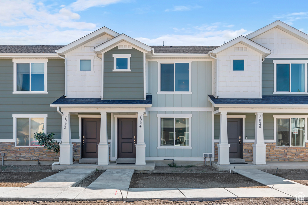 Multi unit property featuring covered porch, roof with shingles, board and batten siding, and stone siding