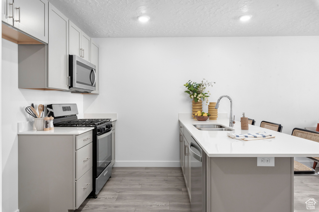 Kitchen featuring a sink, light wood-style floors, a textured ceiling, stainless steel appliances, and a peninsula