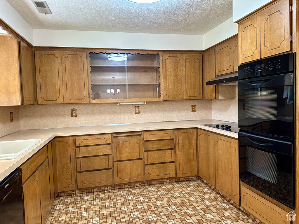 Kitchen with visible vents, light countertops, under cabinet range hood, brown cabinets, and black appliances