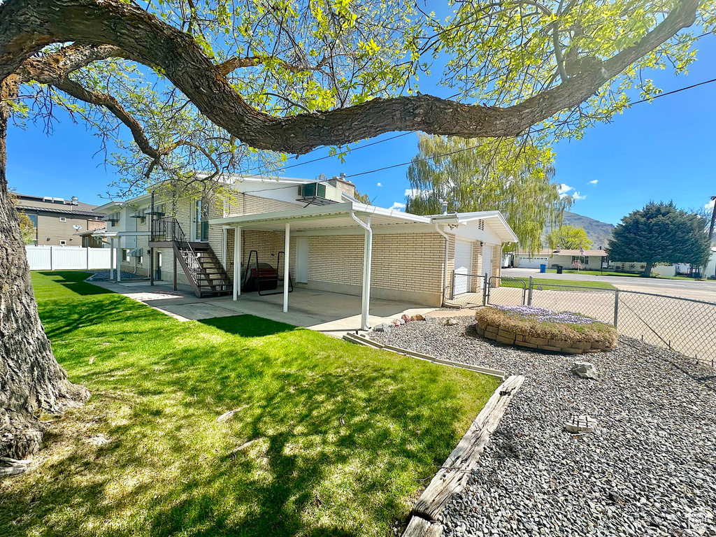 View of home\'s exterior featuring fence, brick siding, a patio area, a lawn, and stairway