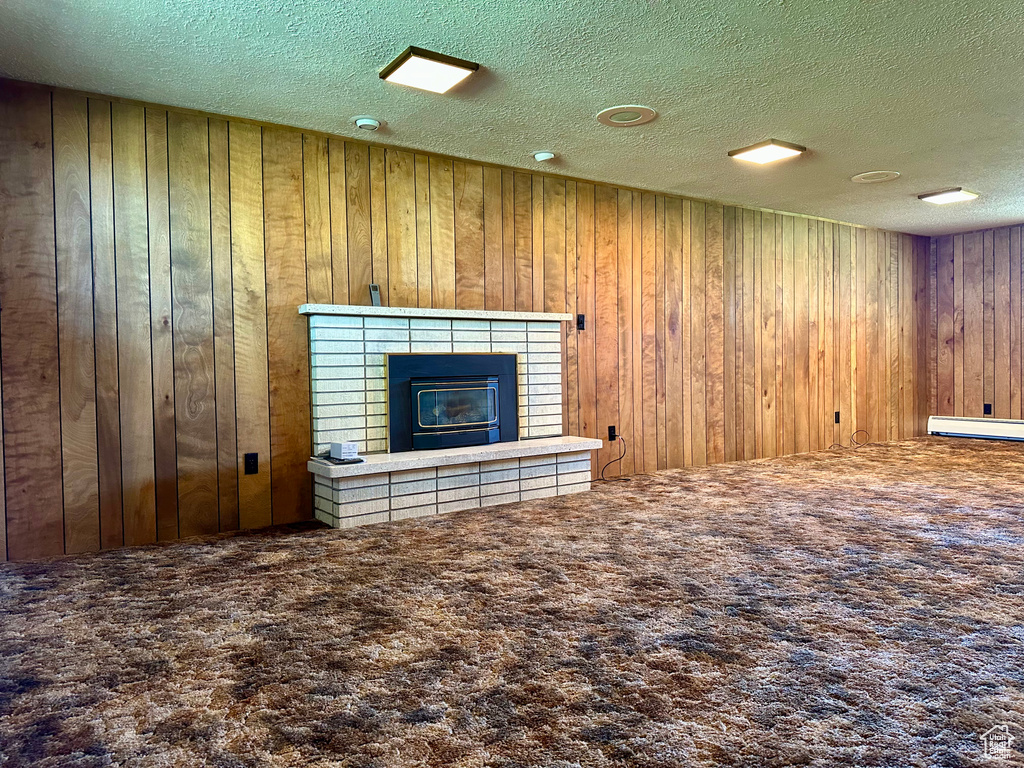 Unfurnished living room with carpet flooring, a textured ceiling, wood walls, and a tile fireplace