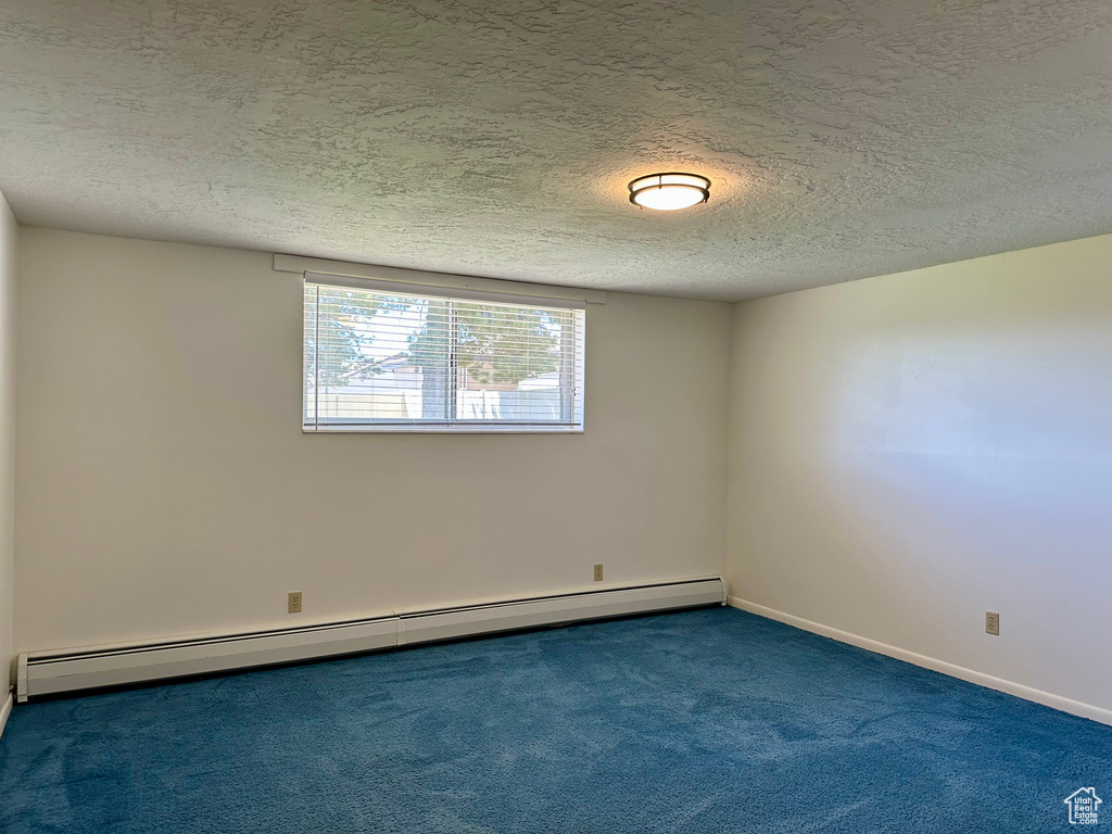 Carpeted empty room featuring baseboards, a baseboard radiator, and a textured ceiling