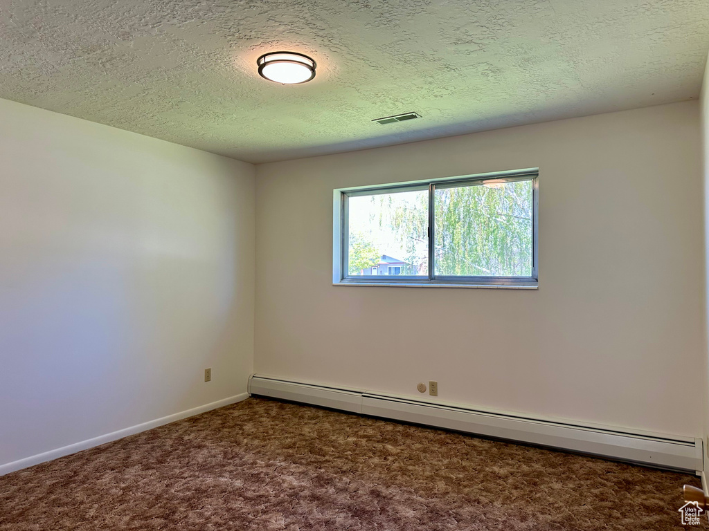 Carpeted empty room featuring baseboards, baseboard heating, a textured ceiling, and visible vents