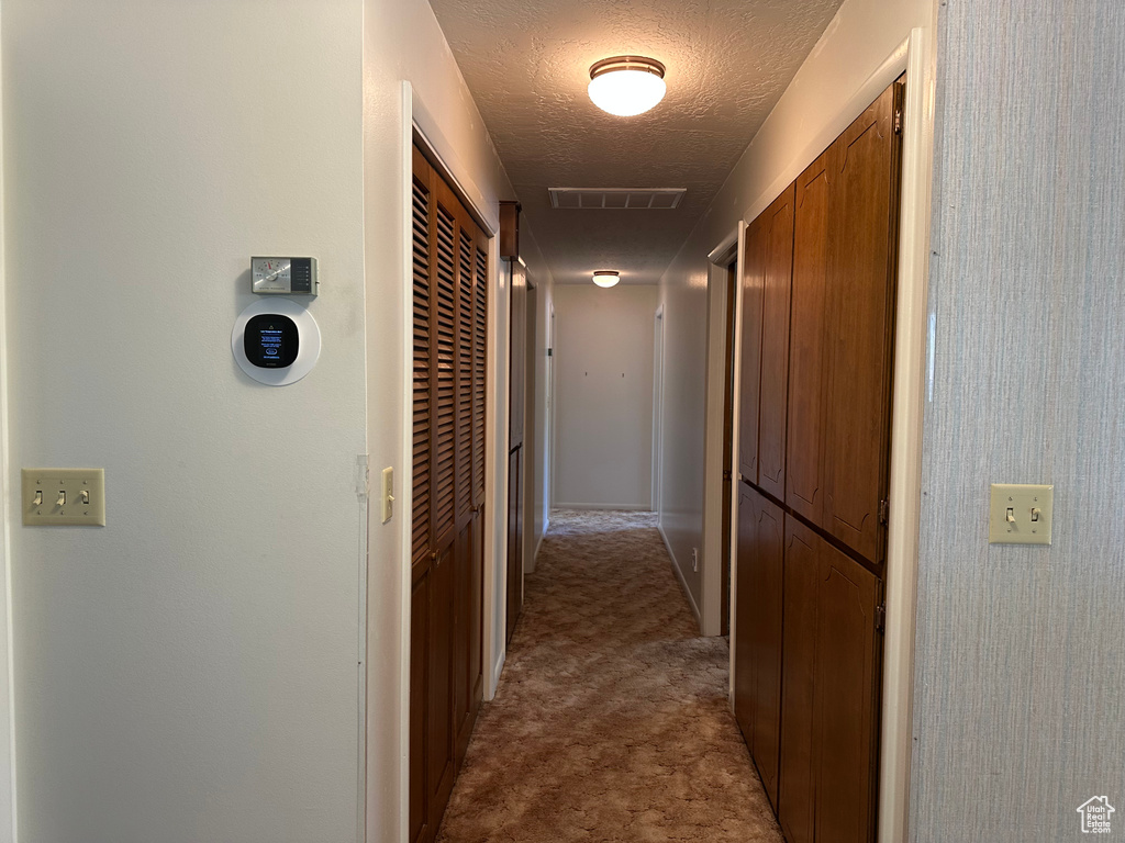 Hallway with visible vents, a textured ceiling, and carpet