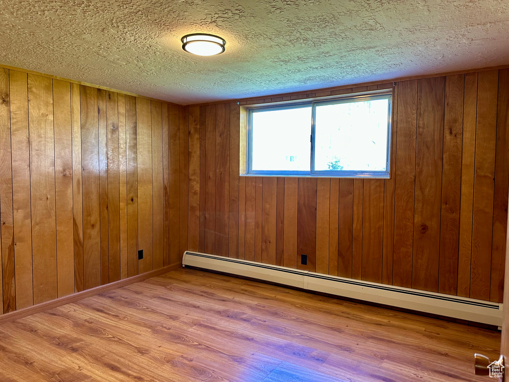 Unfurnished room featuring wood finished floors, a textured ceiling, a baseboard heating unit, and wooden walls