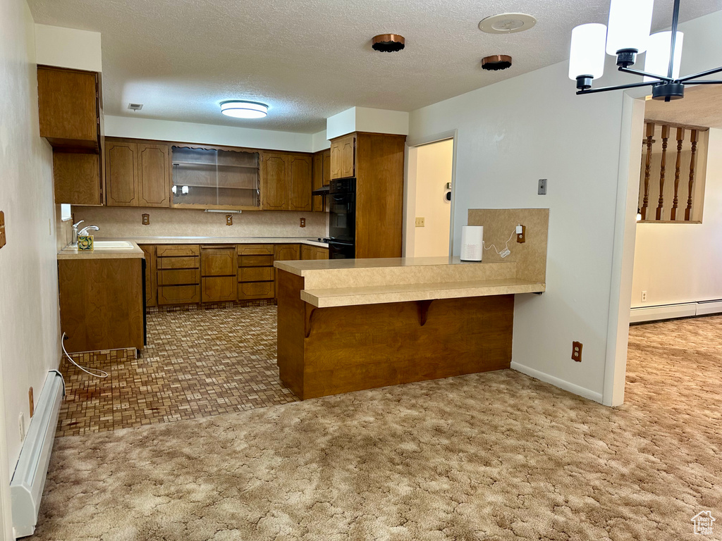Kitchen featuring a peninsula, light countertops, a baseboard heating unit, brown cabinets, and a sink