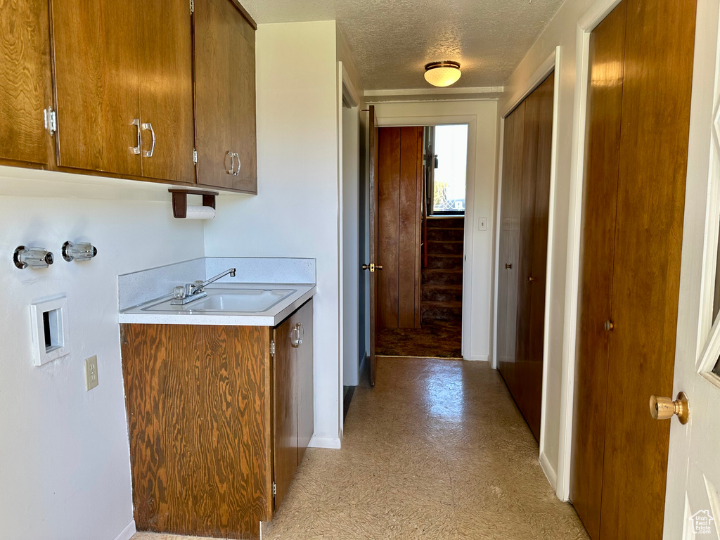 Laundry area with washer hookup, a textured ceiling, cabinet space, a sink, and baseboards