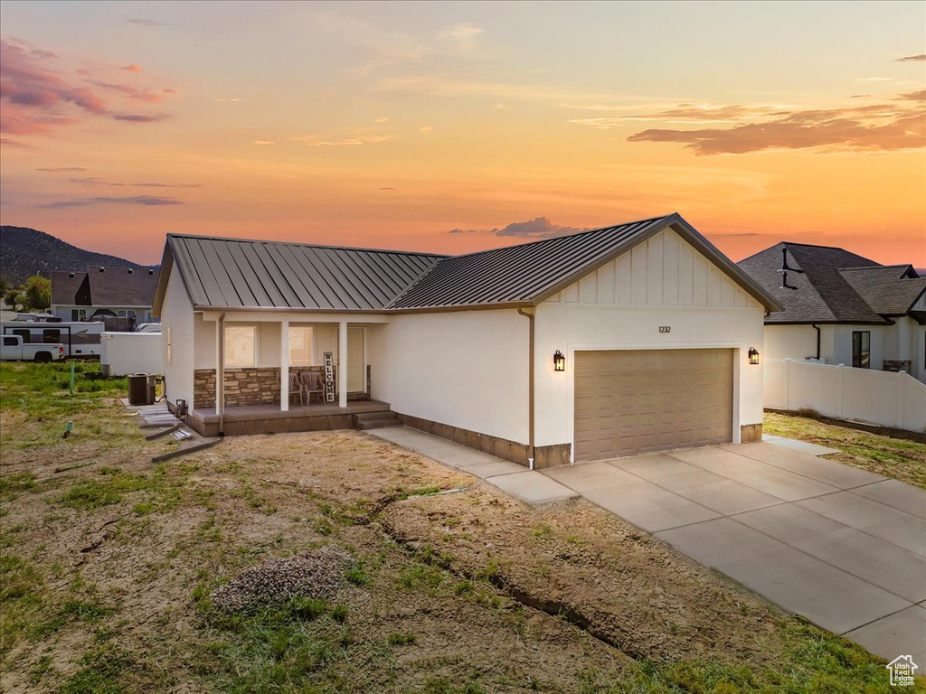 View of front of property with a porch, a standing seam roof, metal roof, driveway, and an attached garage