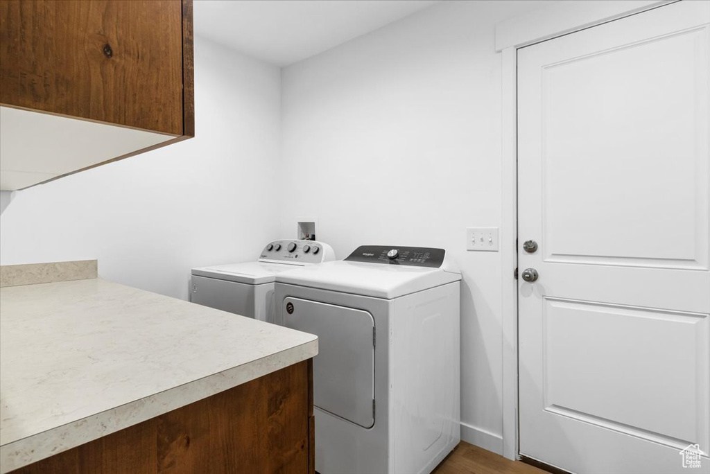 Clothes washing area featuring cabinet space, washing machine and dryer, and light wood-style floors