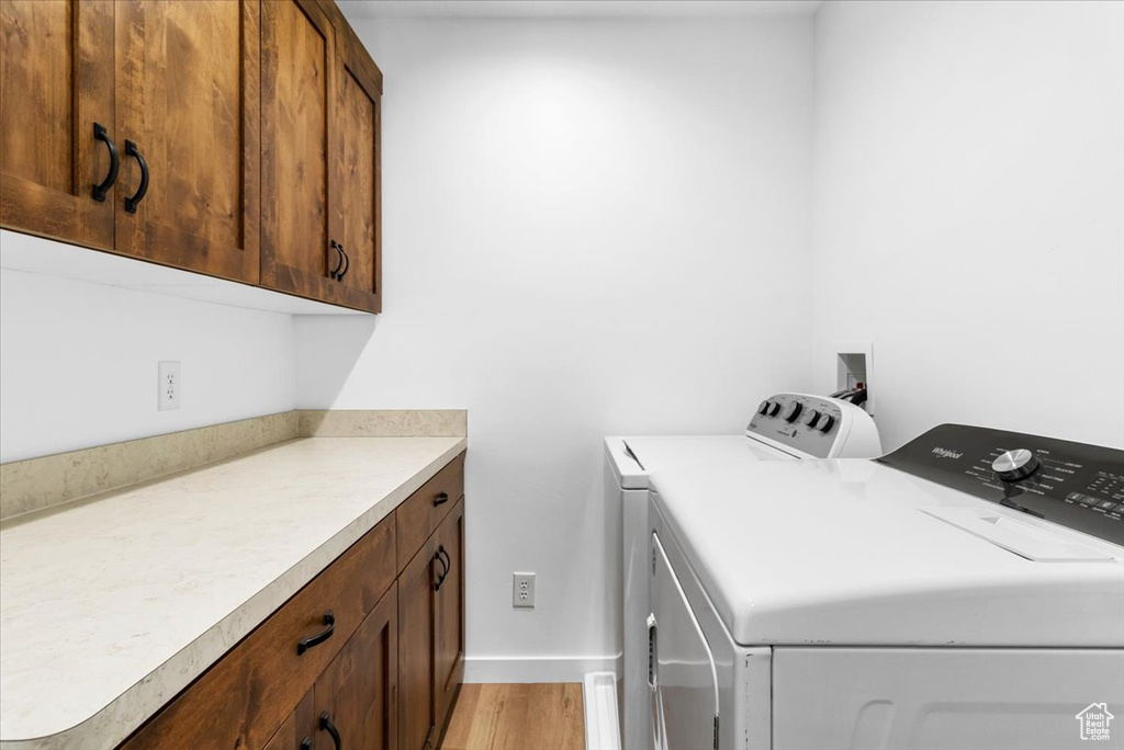 Washroom featuring cabinet space, baseboards, washer and clothes dryer, and light wood-style flooring