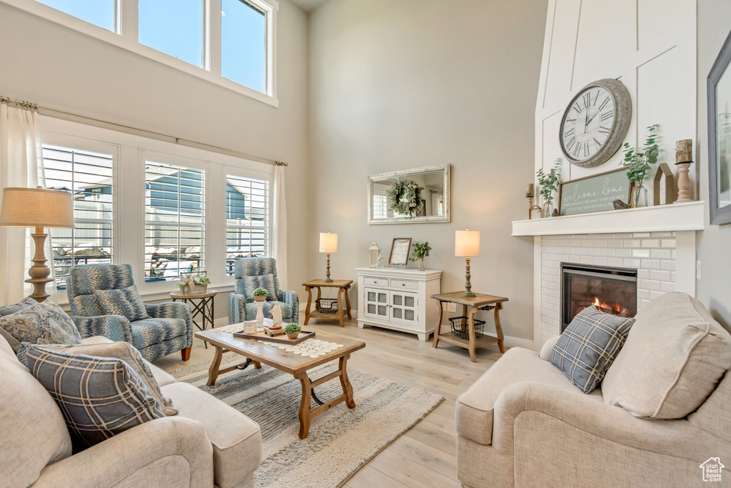 Living area featuring plenty of natural light, a brick fireplace, wood finished floors, and a towering ceiling