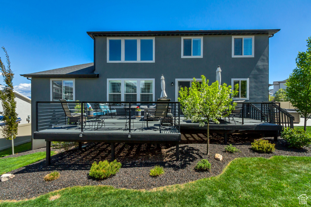 Back of property featuring a lawn, a wooden deck, and stucco siding