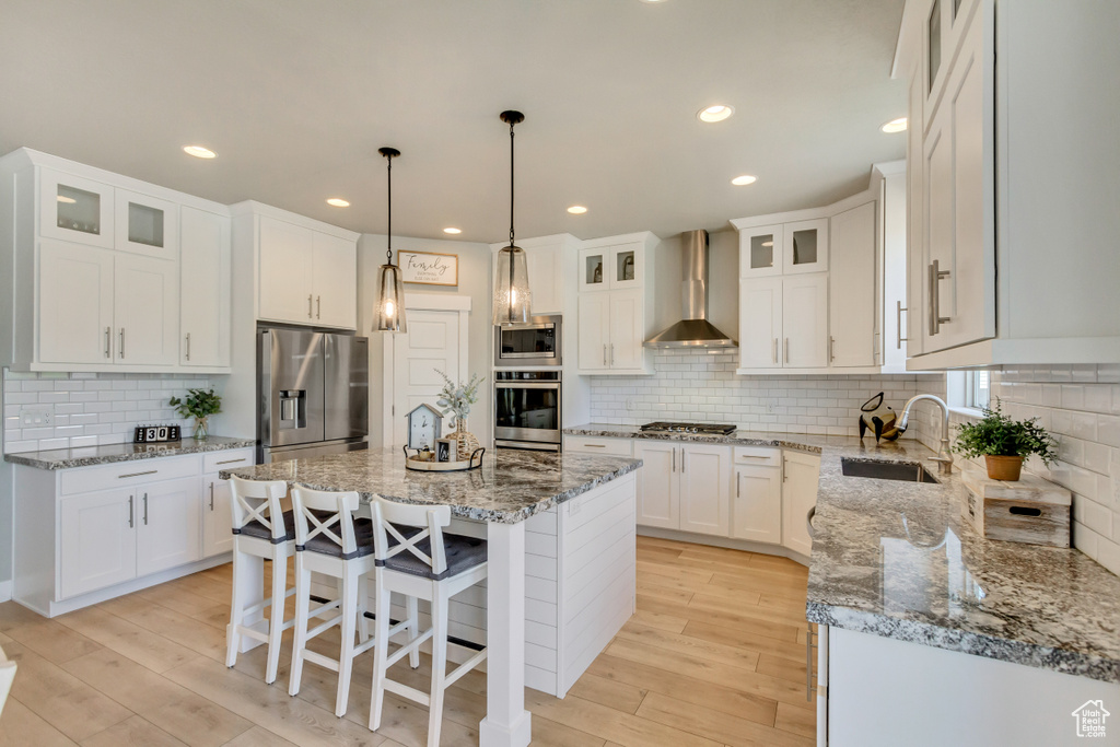 Kitchen featuring wall chimney range hood, a sink, a center island, stainless steel appliances, and backsplash