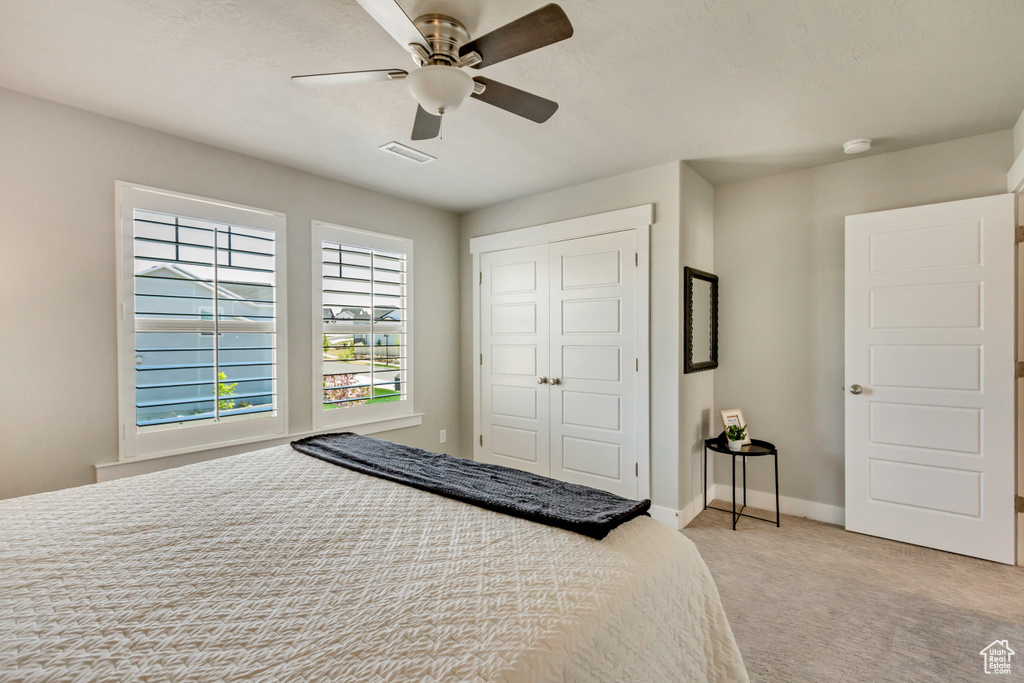 Bedroom with visible vents, a closet, baseboards, light colored carpet, and a ceiling fan